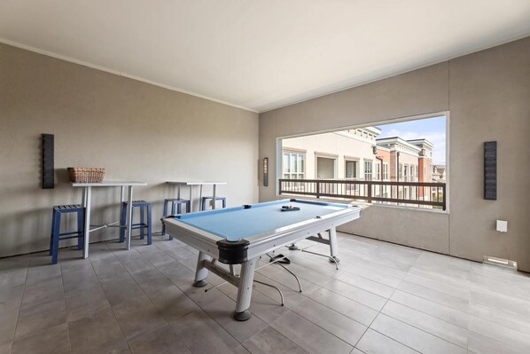 A pool table in a room with a view of buildings through a balcony. - Landing | Beautiful 2BD, Clubhouse, Rooftop Lounge (Fort Worth)
