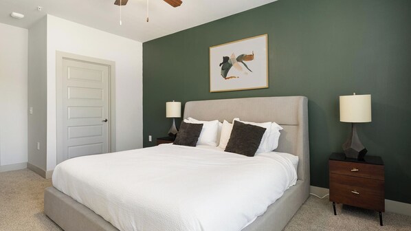 Een slaapkamer met een bed, nachtkastjes, een lamp en een schilderij aan de muur.