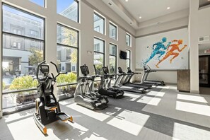 A gym with treadmills, stationary bikes, and a wall mural of running figures. - Landing | Beautiful 2BD, Clubhouse, Rooftop Lounge (Fort Worth)