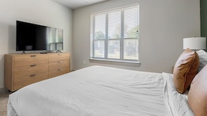 A bedroom with a bed, a dresser, a television, and a window with blinds. - Landing | Amazing 2BD, Rooftop Lounge, Clubhouse (Fort Worth)
