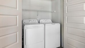 A laundry room with two front-loading washing machines and a metal drying rack above them. - Landing | Amazing 2BD, Rooftop Lounge, Clubhouse (Fort Worth)