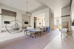 A spacious room with a ping pong table, a hanging chair, and a dining area with chairs and a table. - Landing | Beautiful 2BD, Clubhouse, Rooftop Lounge (Fort Worth)