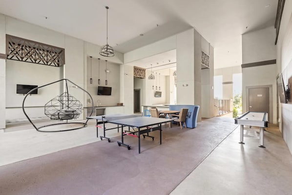 En rummelig stue med et pingpongbord, en hængestol og et spiseområde med stole og bord.