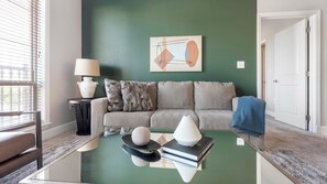 Ein Wohnzimmer mit grüner Wand, einer Couch, einem Couchtisch mit Dekoration, einer Lampe und einer Tür.