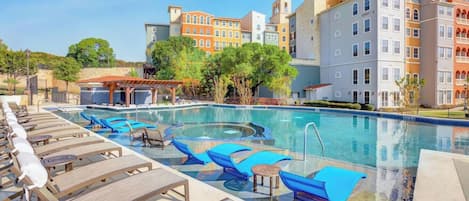 Una piscina con sillas de descanso y una pérgola, rodeada de edificios de varios pisos.