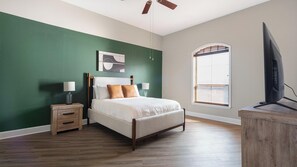Une chambre à coucher avec un lit, des tables de chevet, une télévision et une fenêtre avec des stores.