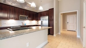 A modern kitchen with dark wood cabinets, stainless steel appliances, and a granite countertop. - Landing | Stylish 1BD, Gym, Courtyard (San Antonio)