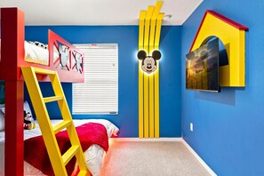 Une chambre d’enfant avec un lit superposé, une décoration murale à l’effigie de Mickey Mouse et un téléviseur fixé au mur.