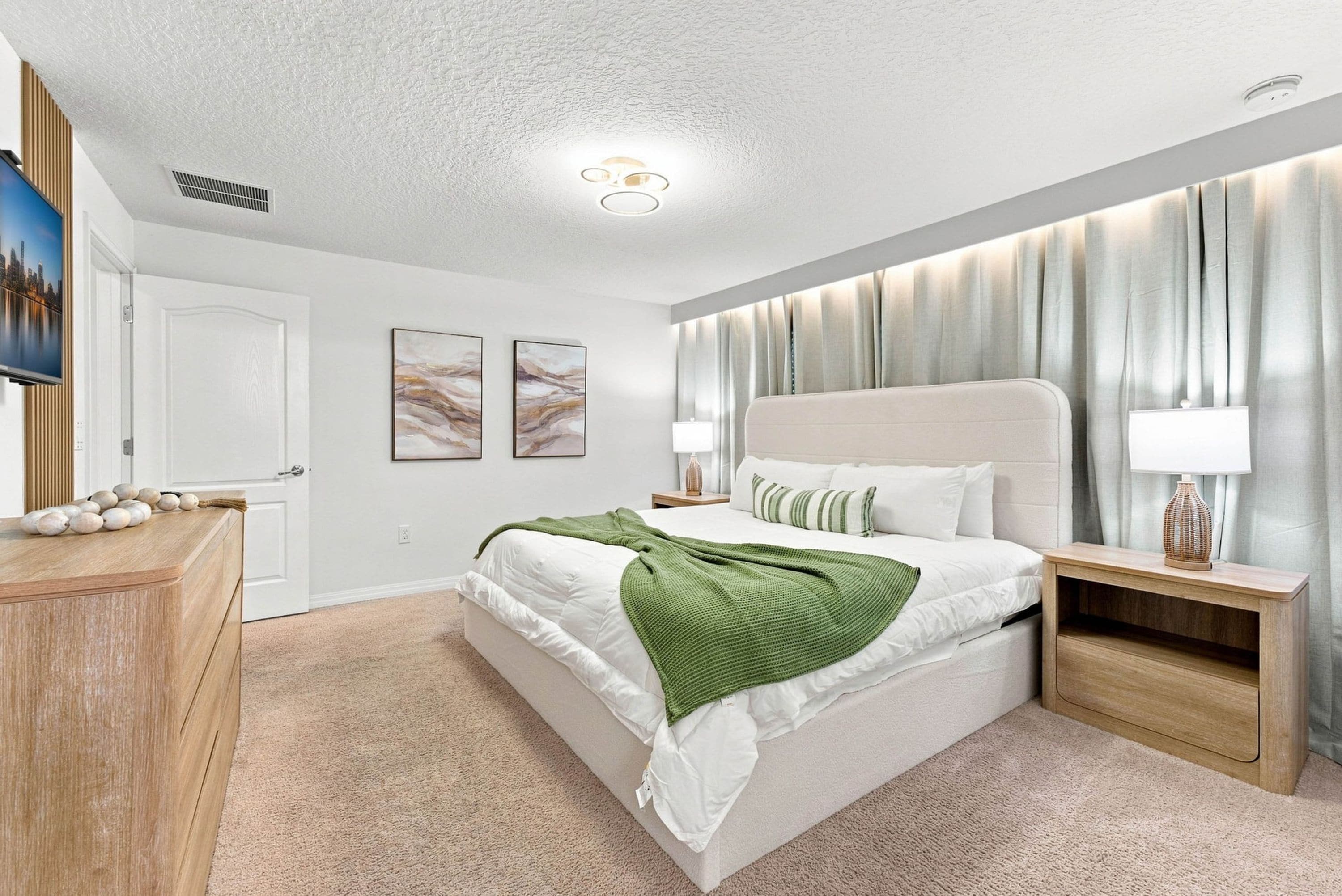 A modern bedroom with a bed, bedside tables, a dresser, and a cityscape artwork on the wall.