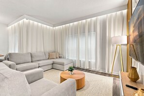 A modern living room with a sectional sofa, a round coffee table, and a large window with sheer curtains.