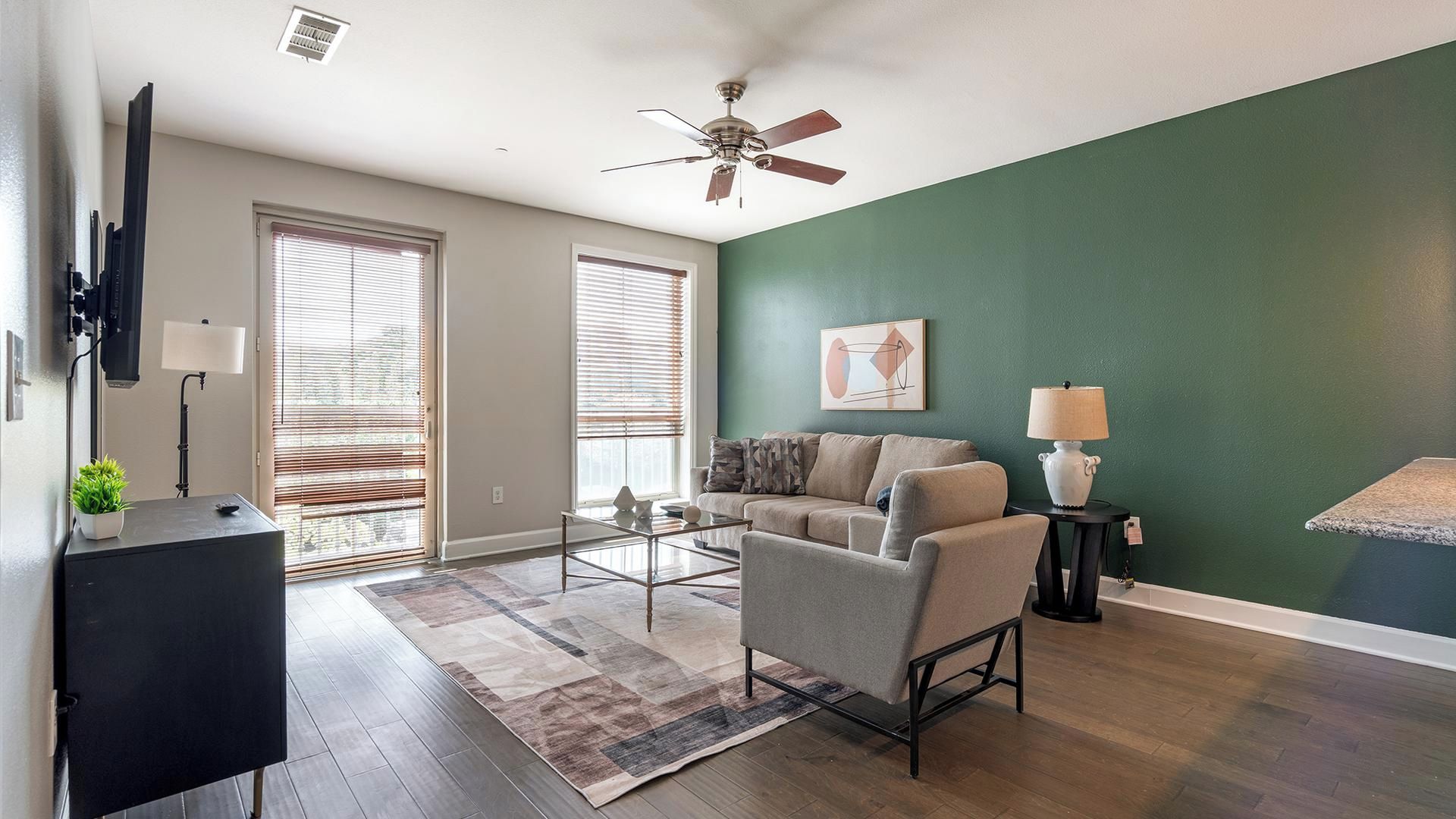 Un salon avec un ventilateur de plafond, un canapé, une table basse et un téléviseur fixé au mur.