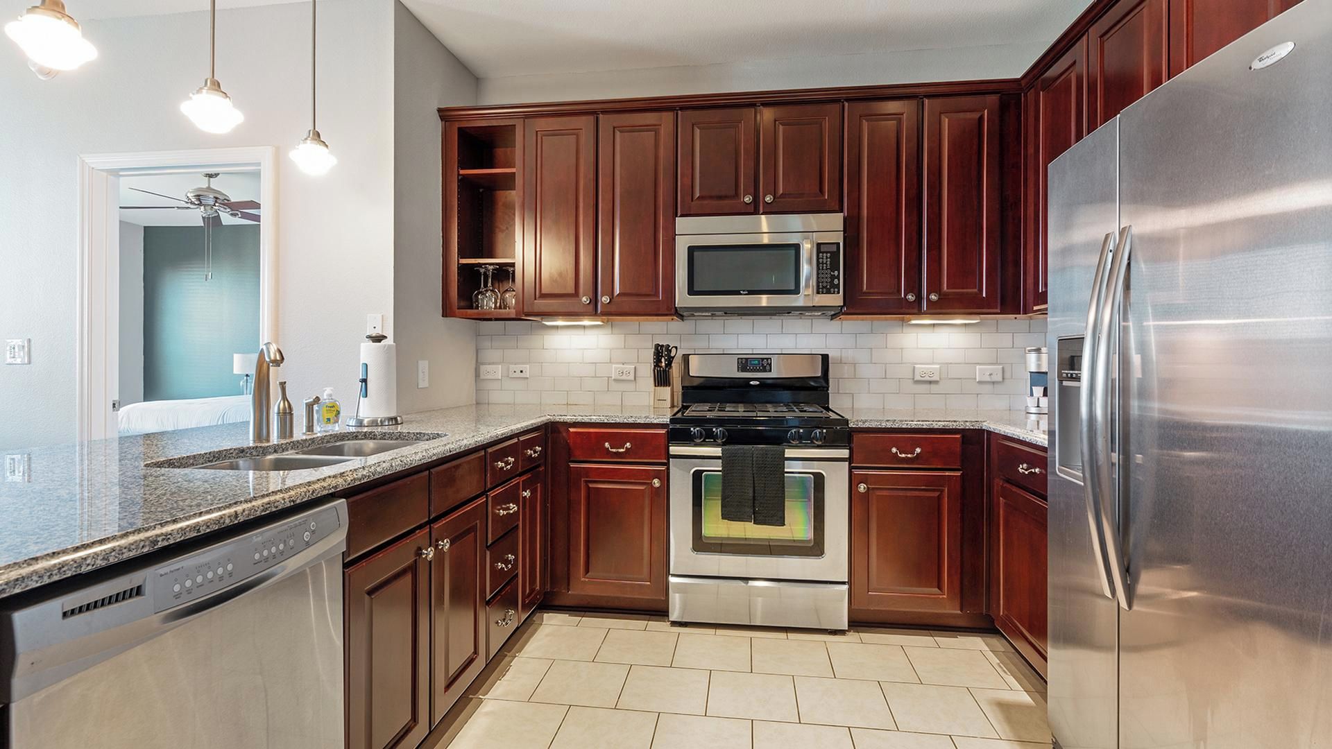 A modern kitchen with stainless steel appliances, wooden cabinets, and a granite countertop.