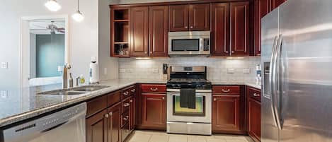 A modern kitchen with stainless steel appliances, wooden cabinets, and a granite countertop.