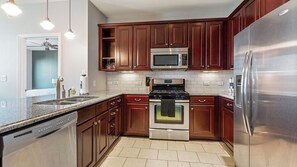 A modern kitchen with stainless steel appliances, wooden cabinets, and a granite countertop. - Landing | Stylish 2BD, Courtyard, Gym (San Antonio)