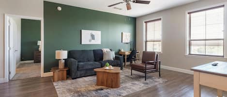 A living room with a dark green wall, a ceiling fan, a sofa, a coffee table, a chair, and a desk with a lamp.