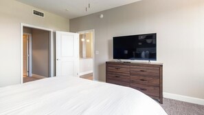A bedroom with a bed, a dresser, a television, and a door leading to another room. - Landing | Stylish 2BD, Courtyard, Gym (San Antonio)