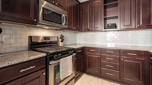 A kitchen with dark wood cabinets, a stainless steel microwave, a gas stove, and a tiled backsplash. - Landing | Amazing 2BD, Gym, Courtyard (San Antonio)