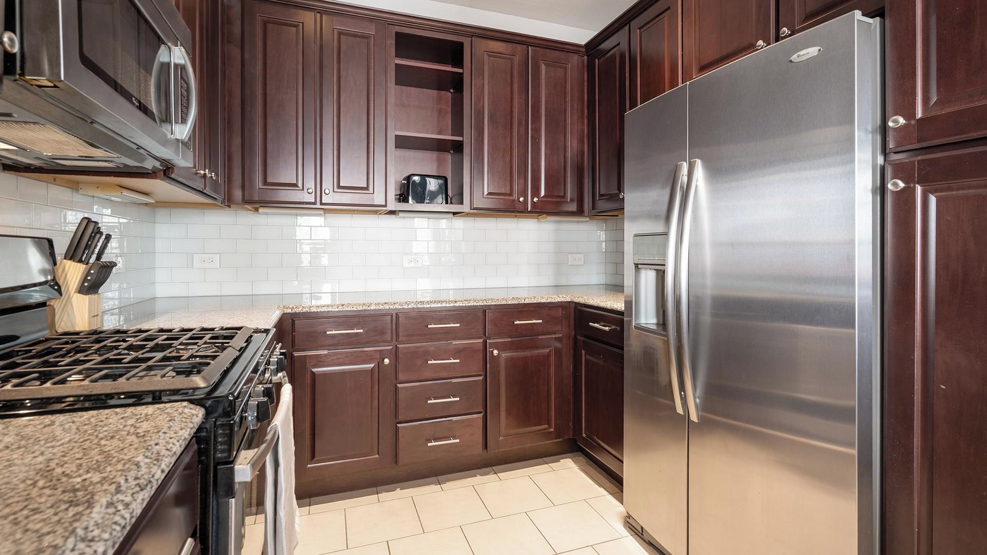 A kitchen with dark wooden cabinets, a stainless steel refrigerator, and a gas stove.