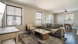 A living room with a sofa, armchair, coffee table, and a dining table with chairs. - Landing | Amazing 2BD, Gym, Courtyard (San Antonio)