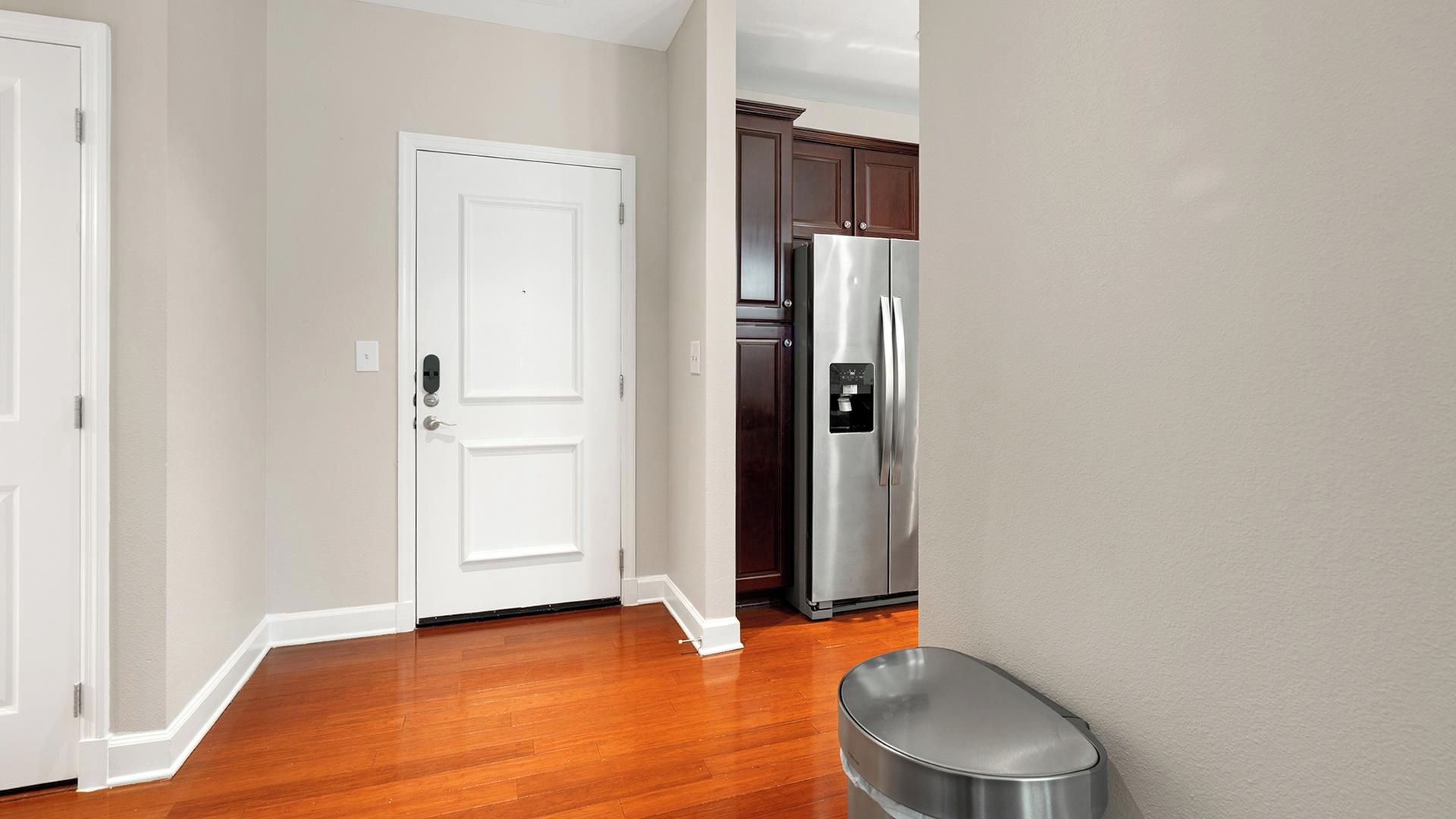 A hallway with wooden flooring, a white door, and a stainless steel refrigerator.