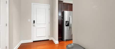 A hallway with wooden flooring, a white door, and a stainless steel refrigerator.