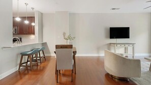 Uma sala de estar moderna com área de jantar, cozinha ao fundo e televisão de tela plana na parede.