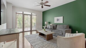 Un salon avec un mur vert, un canapé gris, une table basse, un téléviseur et un ventilateur de plafond.