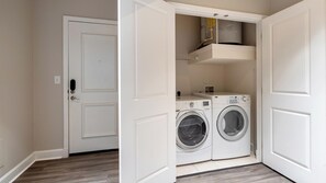 A laundry room with two washing machines and a dryer, a white door, and a small shelf above the machines. - Landing | Spectacular 2BD, Courtyard, Gym (San Antonio)