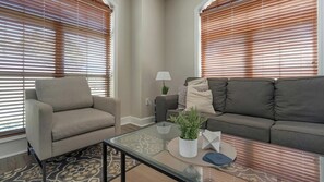 A living room with a sofa, armchair, and a glass coffee table with a plant and decorative items. - Landing | Spectacular 2BD, Gym, Courtyard (San Antonio)