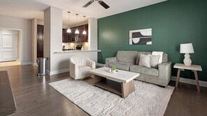 Un salon moderne avec un canapé gris, un fauteuil blanc et une table basse. On peut voir un mur d’accent vert et une porte blanche.