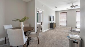 A modern living room with a dining area, a ceiling fan, and a view of a bedroom through an open door. - Landing | Modern 2BD, Gym, Courtyard (San Antonio)