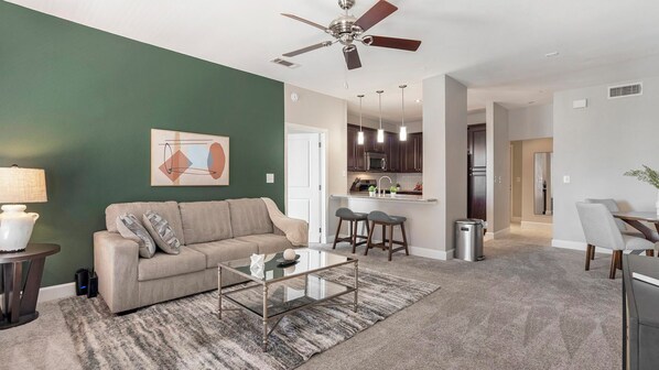 A modern living room with a sofa, coffee table, and a ceiling fan. - Landing | Modern 2BD, Gym, Courtyard (San Antonio)