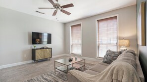 Ein Wohnzimmer mit Deckenventilator, einem Wand-Fernseher, einer Couch mit Überwurfdecke und einem Couchtisch.