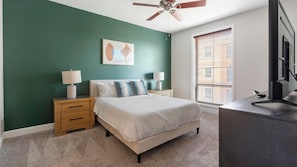 A bedroom with a bed, two bedside tables with lamps, a ceiling fan, a window with blinds, and a TV on a dresser. - Landing | Modern 2BD, Gym, Courtyard (San Antonio)