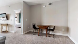A room with a carpeted floor, a wooden table with two chairs, a television on a stand, and a door leading to another room. - Landing | Amazing 1BD, Gym, Courtyard (San Antonio)
