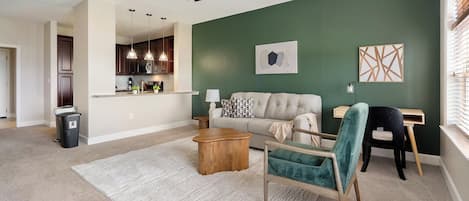 A living room with a sofa, a chair, a coffee table, and a dining area with a kitchen in the background.