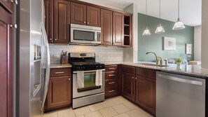 A modern kitchen with stainless steel appliances, wooden cabinets, and pendant lighting. - Landing | Amazing 1BD, Gym, Courtyard (San Antonio)