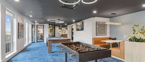 A room with a foosball table, a billiards table, and a seating area with a table and chairs.