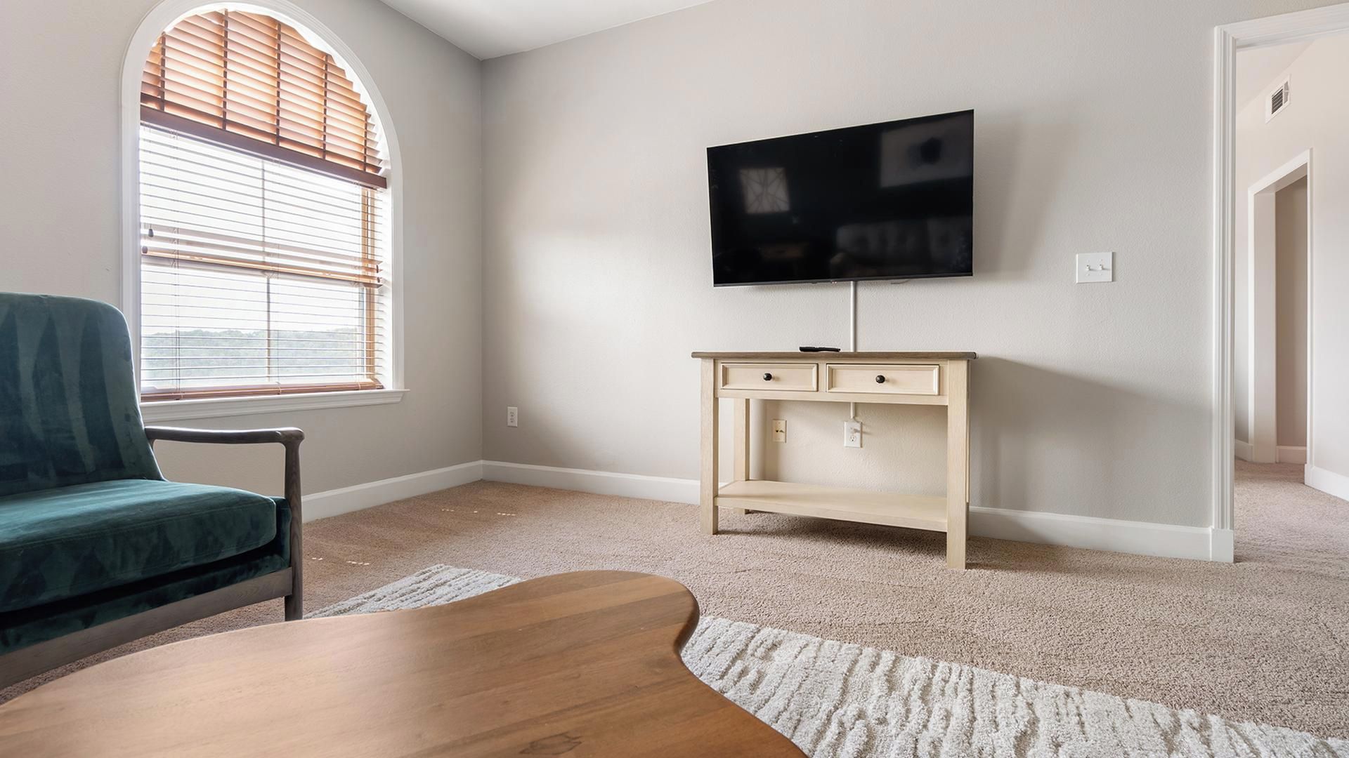 A living room with a television, a sofa, a wooden coffee table, and a window with blinds.