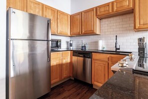 A modern kitchen with wooden cabinets, stainless steel appliances, and a marble countertop. - Landing | Incredible 1BD, Gym, Pool (Kansas City)