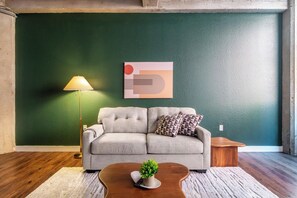 A living room with a sofa, a lamp, a coffee table with a plant, and a wall with a geometric painting. - Landing | Incredible 1BD, Gym, Pool (Kansas City)