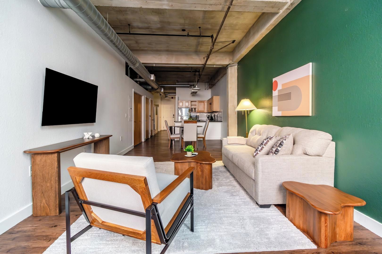 A modern living room with a sofa, coffee table, and armchair, a flat-screen TV, and a kitchen in the background.