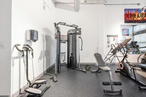 Ein Fitnessraum mit Trainingsgeräten, einer Sitzbank und einem an der Wand montierten Fernseher.