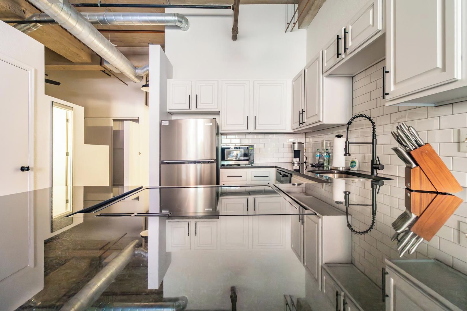 A modern kitchen with stainless steel appliances, white cabinetry, and a reflective backsplash.