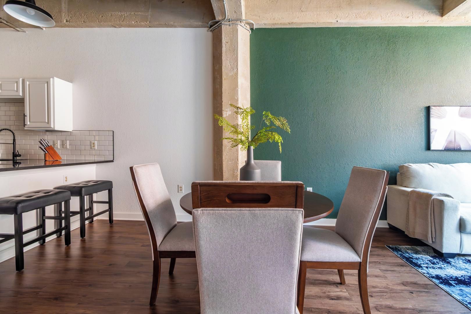 Une cuisine moderne avec des meubles blancs, un plan de travail noir et un coin repas comprenant une table ronde et des chaises.