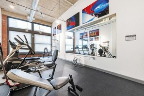A gym with exercise equipment, large windows, and artwork on the walls. - Landing | Stylish 1BD, Gym, Pool (Kansas City)