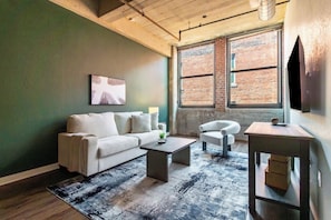 A living room with a sofa, armchair, coffee table, and a TV on a stand. - Landing | Stylish 1BD, Gym, Pool (Kansas City)
