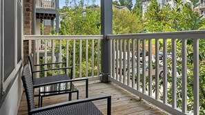 A balcony with two chairs and a table, overlooking a street with parked cars and residential buildings.