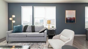 A living room with a grey sofa, a white armchair, a floor lamp, and a painting on the wall. - Landing | Incredible 2BD, Gym (Gainesville)