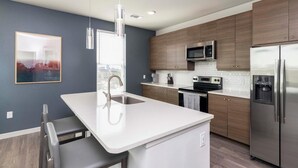 A modern kitchen with a white island, stainless steel appliances, and wooden cabinets. - Landing | Incredible 2BD, Gym (Gainesville)